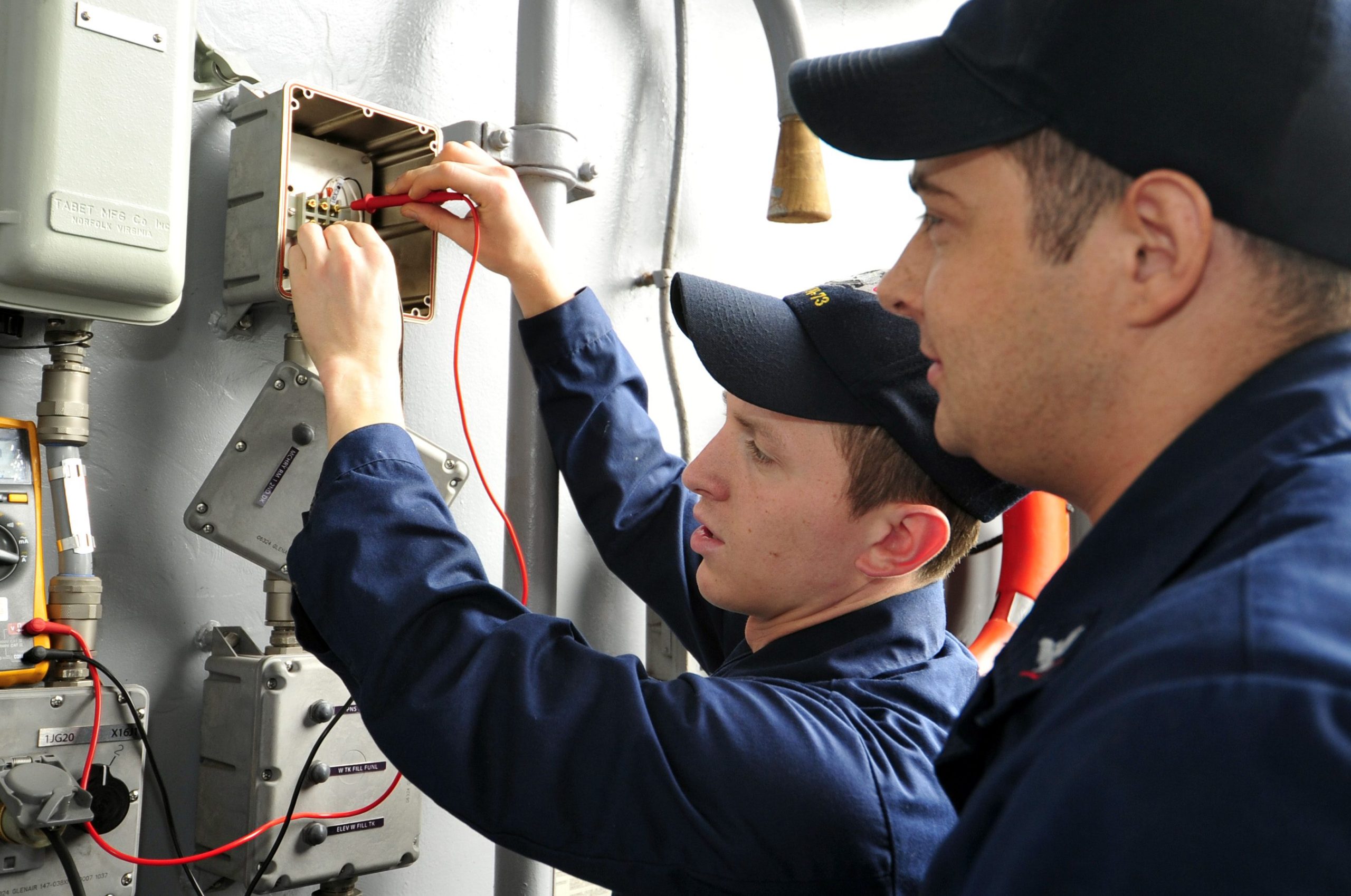 Expert electricians diagnosing industrial electrical components with a multimeter to ensure system safety and efficiency.