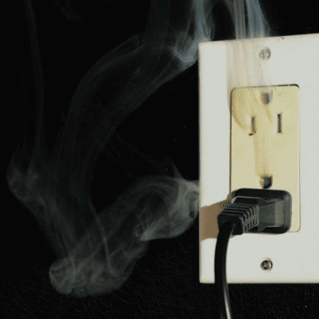 Smoke rising from a damaged wall outlet, indicating a dangerous electrical short and need for emergency repair.